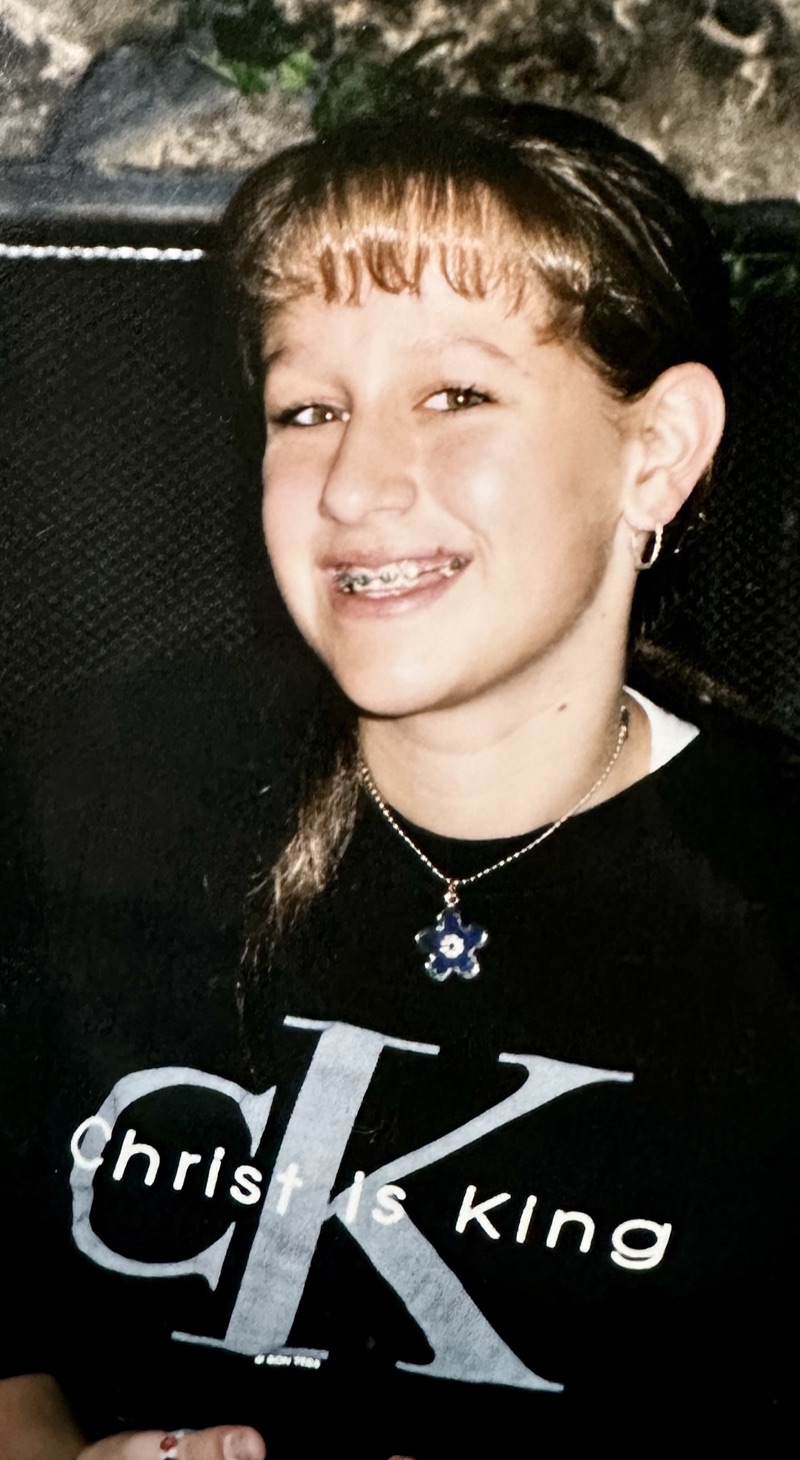 Carrie as a kid with braces, wearing a black t-shirt with the Calvin Klein logo altered to read Christ is King